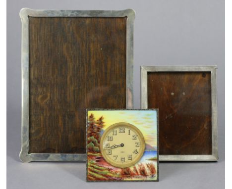 An enamelled white metal square bedside timepiece painted with a wooded lake scene, with easel support, 3½” wide; a silver re