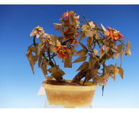 A CHINESE HARDSTONE FLOWERING TREE IN AN OCHRE AND GREY HARDSTONE ELONGATED OVAL TROUGH.   H 21cms.