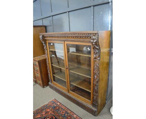 Late Victorian gothic carved oak bookcase cabinet with two glazed doors, later panelling to sides, 143cm wide