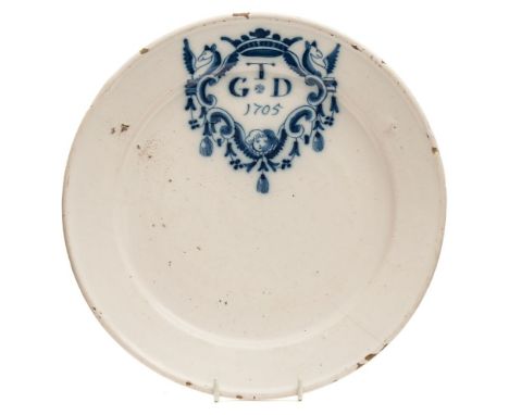 An early 18th century dated delftware marriage plate: painted in blue with a 'merryman' style cartouche of winged griffons, a