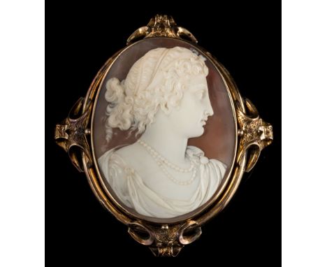 A late 19th century oval shell cameo portrait brooch: the oval shell cameo 54mm long x 41mm wide depicting a woman, her hair 