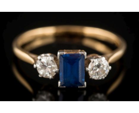 An 18ct gold, sapphire and diamond three-stone ring: the rectangular sapphire 6mm long x 4.2mm wide, in four claw setting bet