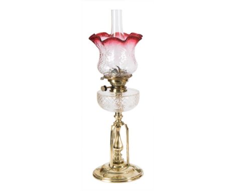An Arts & Crafts influence brass oil lamp: with Hicks No 2 Lever wick holder, having a clear glass circular reservoir, raised