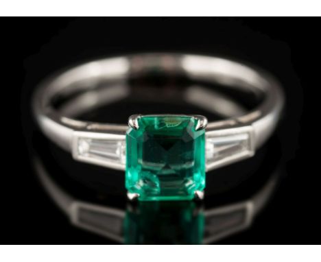 An emerald and diamond ring: the rectangular-cut emerald estimated to weigh 0.69ct and between tapered baguette-cut diamond s