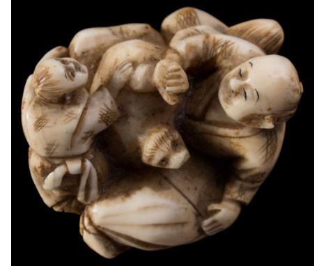 A Japanese carved ivory netsuke, signed Gyokubun: of a seated man and crouching boy playing with a dog or badger, Meiji, 4.5 