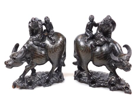A pair of Chinese ebonised hardwood carved buffalo figures, each with a repeat scroll decoration, set with figures to their b