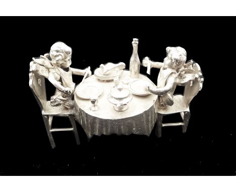 Early 20th century German Hanau silver miniature, modelled as two putti feasting at a dining table laden with food and drink,