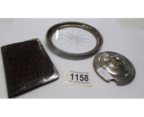 A glass coaster with silver rim, a card case with silver corners and a silver jam pot lid.