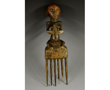 Tribal Art - a Luba comb, carved as a female figure seated astride a six-prong lower section, 27cm high, Congo, 19th century 