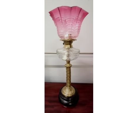 A 19th century Corinthian column oil lamp having a cranberry glass shade above stylized thistle support and base