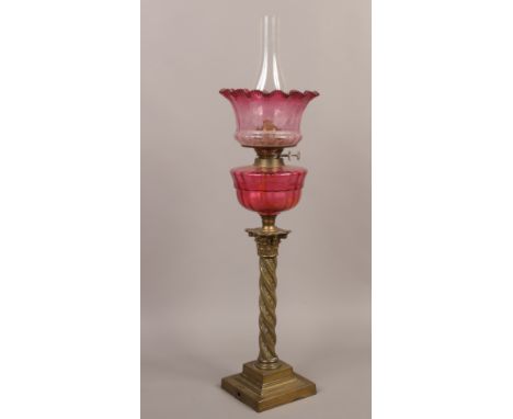 A Victorian cranberry glass twin burner oil lamp with engraved shade raised over a twisted brass column.Condition report inte