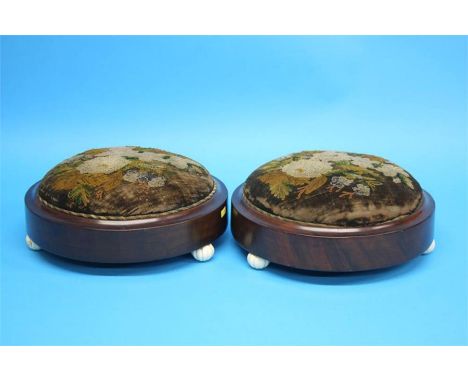 A pair of Victorian walnut circular foot stools with upholstered tops and supported on white ceramic feet.  29 cm diameter