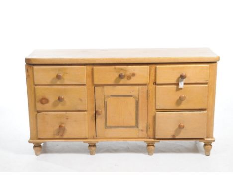 A Victorian pine kitchen dresser baseWith a slab top over an arrangement over seven drawers and a central cupboard door, rais