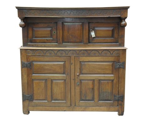 A 17th Century oak court cupboardWith a geometric " C " scroll carved frieze above two sphere finials and a pair of panelled 