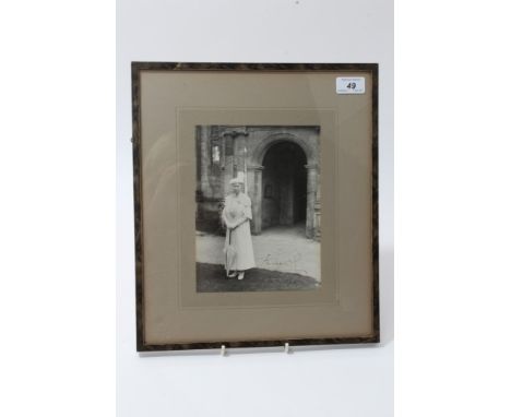 HM Queen Mary - signed presentation photograph of Her Majesty in white dress and hat, with white parasol, standing outside a 