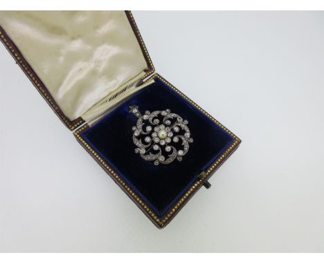 of pierced circular form, set to the centre with a 4mm pearl in a border of old round brilliant cut diamonds, and open scroll