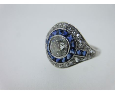with a central old round brilliant cut diamond (estimated weight 0.85cts) in a halo of channel set shaped calibré cut sapphir