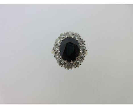 the oval cut midnight blue sapphire claw set to a close border of twelve round brilliant cut diamonds, plain tapered shank si