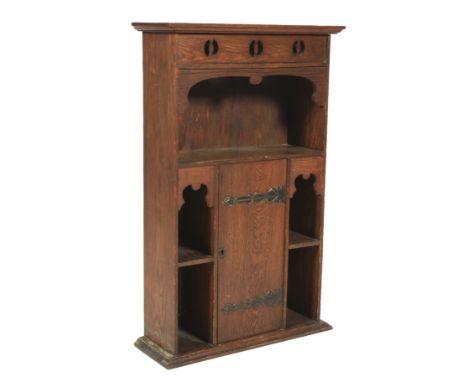 An oak Liberty style hanging bookcase. With pierced decoration to the pelmit above a shaped shelf. The lower section with cen