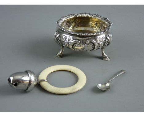 A VICTORIAN SILVER SALT and a 1920's baby's rattle, the circular salt with floral decoration in relief on three hoof feet, st