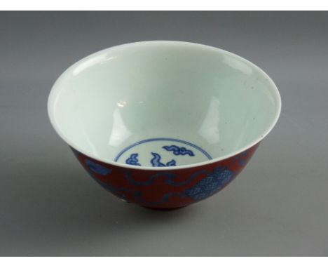 A CHINESE CORAL GROUND PORCELAIN BOWL decorated with underglazed blue mythical lions having ribbons in their mouths attached 