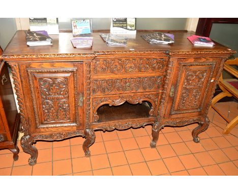 AN EARLY 20TH CENTURY HEAVILY CARVED OAK SIDEBOARD, with two foliate decorated panelled doors flanking two drawers above an o