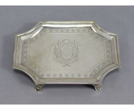 A George III silver teapot stand of rectangular shape with re-entrant corners &amp; engraved borders, an armorial to the cent