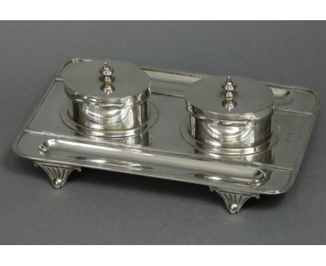 An Edwardian silver desk inkstand of rectangular form with reeded rims, a pen-trough either side, fitted two oval straight-si