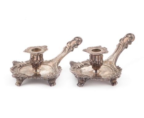 A pair of George III silver chamber candlesticks, each of shaped form, with a rococo border, raised on four scrolled feet and