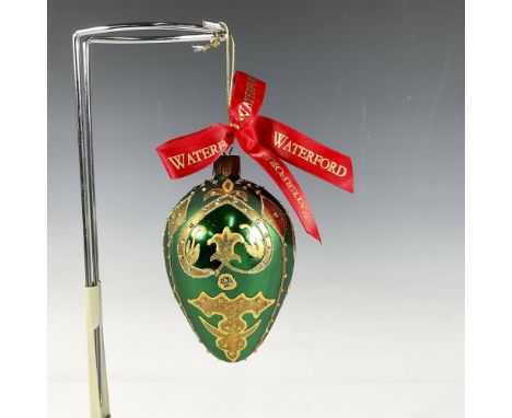 Handcrafted ornament adorned with gold decorative elements that include holly leaves and a stylized fleur de lis crown. The s