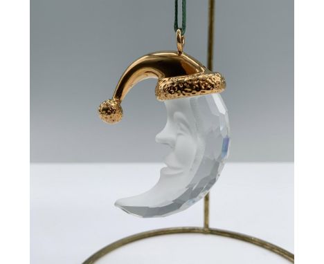 A crescent moon with a frosted face, adorned with a gold-colored Christmas hat. Swarovski backstamp. This item has its origin