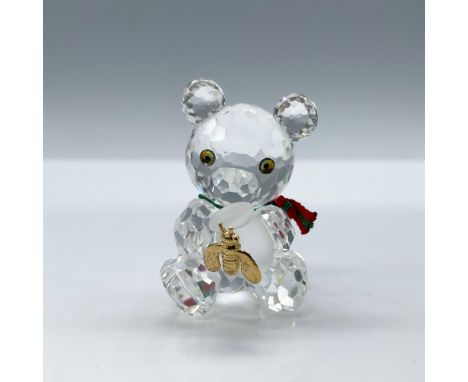 A clear crystal figure of a bear sitting down on their bottom while holding a honey pot that is decorated with a gold-colored