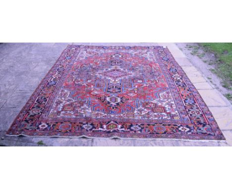 A Persian Heriz carpet, with central medallion geometric motifs on a red ground within a multi border, 321 x 258 cm