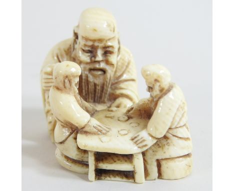 A Japanese carved ivory netsuke, of three figures seated around a table, signed to base, 4cm high