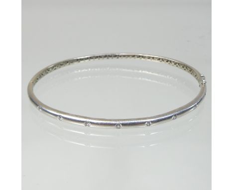 A 9 carat gold and diamond set bangle, of hinged shape set with a row of nine diamonds, approximately 0.45 carats gross