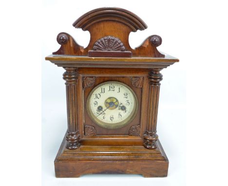 An oak mantel clock with shaped pediment above circular dial set with Arabic numerals flanked by fluted column, height 38cm.