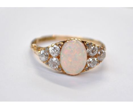 An Edwardian 18ct yellow gold ring set with oval opal cabochon flanked by six diamonds to the triangular shanks, each stone a