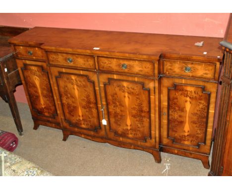 A reproduction yew breakfront sideboard of slender proportions with four short drawers above four cupboard doors to bracket f