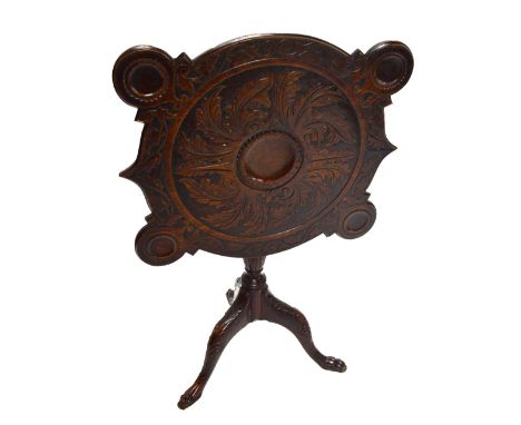 A George III Irish mahogany tilt-top games table, carved with foliate motifs to the top, with dished corners, on turned balus