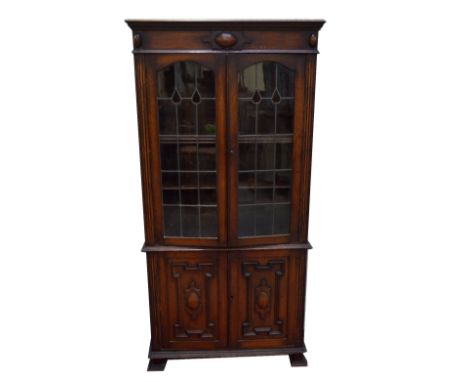 An early 20th century oak bookcase with pair of leaded glazed doors enclosing adjustable shelves above a pair of cupboard doo