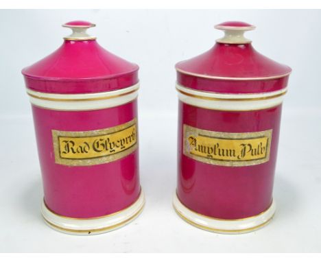 A pair of Shaw & Sons ceramic cylindrical pharmaceutical jars with gilt heightened borders and painted in dark pink, with lab
