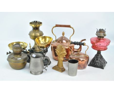 A small group of metalware to include two graduated copper kettles, a cast iron oil lamp with ruby glass reservoir, a door st