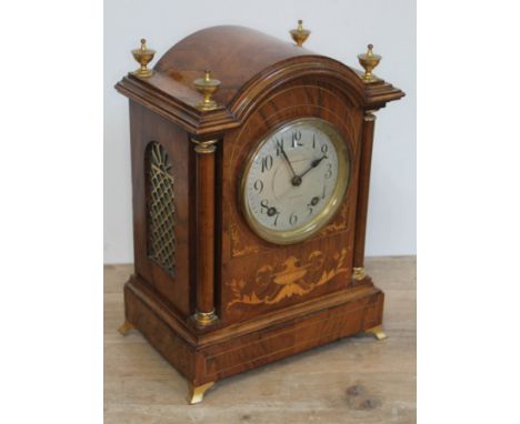 An Edwardian walnut mantle clock with domed top, brass finials, marquetry inlay, columns, fish grille panels and brass bracke