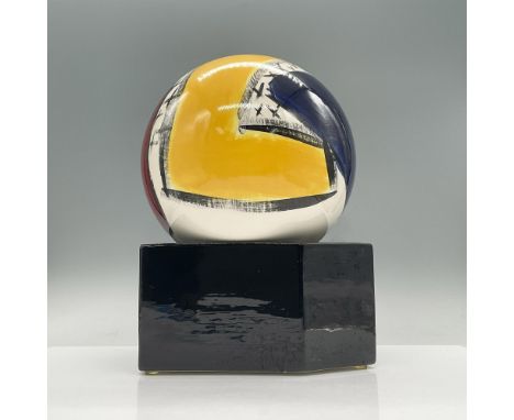 Glossy ceramic sphere with an abstract pattern rendered in black, white and primary colors. Sphere sits on a black geometric 