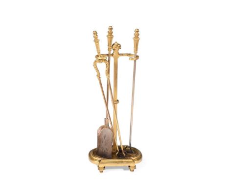 A FRENCH GILT METAL FIRESIDE COMPANION SET  CIRCA 1890-1910  Comprising a set of three fire tools and stand, richly decorated