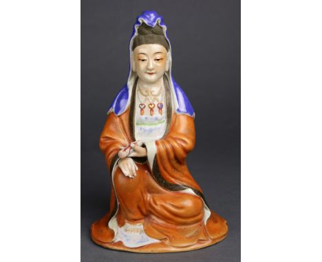 A Chinese ceramic seated figure of Guanyin, wearing beaded necklace and long ornate robes with a shawl over the high chignon,