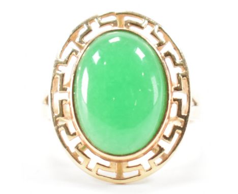 A vintage gold and jade cabochon ring. The ring set with a central jade cabochon framed by pierced decorated mount. Stamped 1