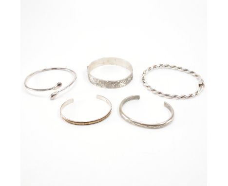 A group of four silver and one white metal bangle. The lot to include a wrap around bangle (marked 925), an open bangle with 