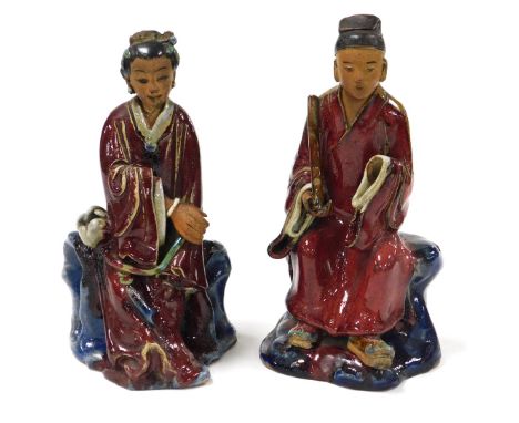 A pair of Chinese red glazed and buff stoneware figures, of a seated gentleman, and lady, the gentleman holding a scroll, lad