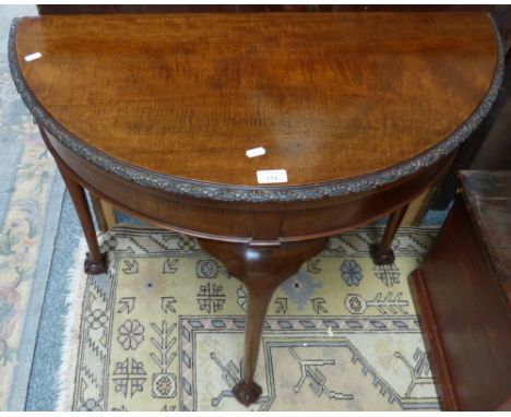 An early 20th century mahogany half round fold-over card table, with carved edge, pull-out drawer and four cabriole legs with